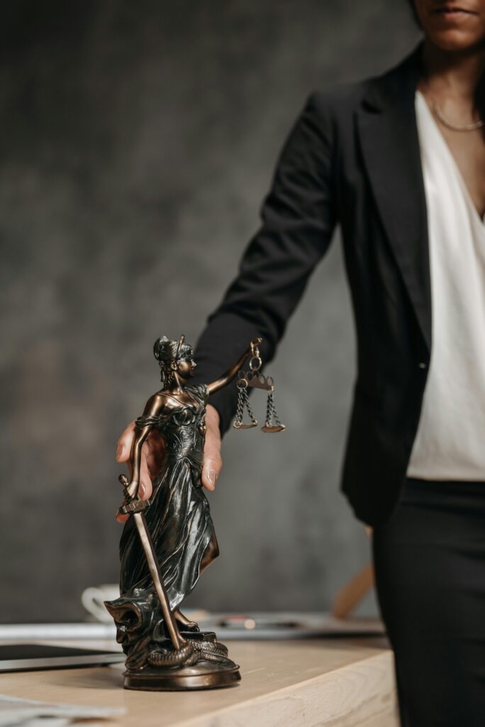 A professional woman holds a bronze Lady Justice figurine on a desk, symbolizing legal justice.